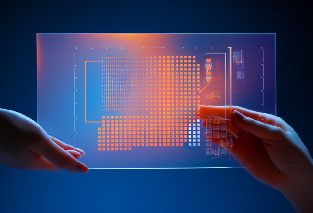 Das Bild zeigt zwei Hände, die ein transparentes, leuchtendes Display halten. Das Display enthält verschiedene geometrische Muster und Diagramme in leuchtenden Farben wie Orange und Blau. Es scheint sich um eine futuristische oder technologische Benutzeroberfläche zu handeln, möglicherweise in einem Kontext der Datenanalyse oder der digitalen Visualisierung.