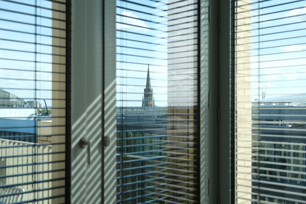 Ein Blick auf eine Stadt aus einem Fenster mit Jalousien, wo Inhalt auf urbane Landschaft trifft.